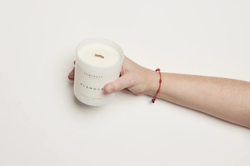 Hand holding a white candle labeled 'Glamour' on a light background